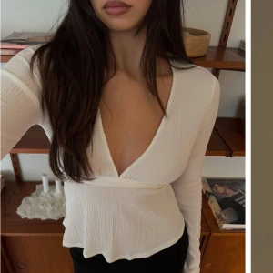 Vit ribbad omlottopp - Snygg vit ribbad omlottopp med lång ärm och djup v-ringning. Toppen har en knytning i ryggen som ger en fin passform. Perfekt för en stilren look.