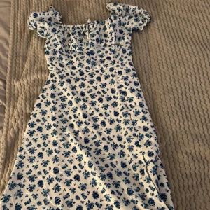 Blommig klänning med puffärmar - Superfin klänning med blått blommönster på vit bakgrund. Den har söta puffärmar och en smickrande passform. Perfekt för sommarens alla fester. Klänningen är i mycket bra skick 