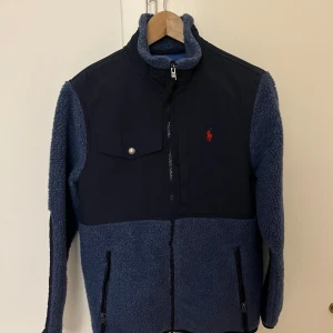Blå fleecejacka från Polo Ralph Lauren - Säljer en snygg och varm blå fleecejacka från Polo Ralph Lauren.  Den är perfekt för kyliga höst- och vinterdagar. Jackans storlek är XS och nypris är runt 3000kr