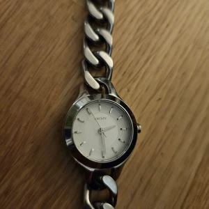 Silverfärgad klocka från DKNY - Säljer en stilren och elegant klocka från DKNY i silverfärg. Klockan har en klassisk länkarmband och en vit urtavla med minimalistiska markeringar. Perfekt för både vardag och fest. Den är i bra skick och redo att användas direkt. Passa på att köpa denna snygga accessoar! ✨