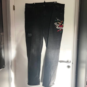  Jeans från Ed Hardy - Säljer ett par svarta jeans från Ed Hardy med coolt broderi av en fågel och texten 'True Death' på benet. Jeansen har en straight passform och är i bra skick. Midjemått tvärsöver: 53cm 