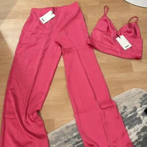 Rosa byxdress med topp - Säljer en snygg rosa byxdress med matchande topp. Byxorna har en loose passform och är högmidjade, vilket ger en bekväm och trendig look. Perfekt för sommarens fester eller en dag på stan. Materialet känns mjukt och skönt mot huden.