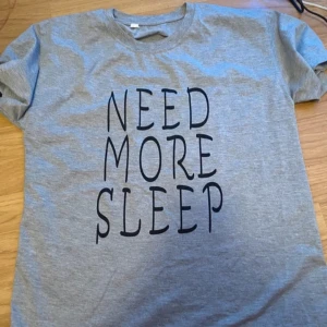 Grå t-shirt med text - Säljer en grå t-shirt med texten 'NEED MORE SLEEP' i svart. Perfekt för en avslappnad stil eller som en rolig present. T-shirten är i bomull och har en normal passform med korta ärmar. Perfekt för vardagsbruk eller som en pyjamastopp.