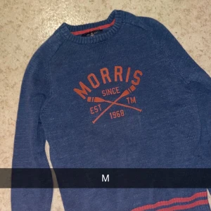 Blå tröja från Morris - Säljer en snygg blå tröja från Morris med orange text och detaljer. Perfekt för en casual look. Tröjan har långa ärmar och är i mycket bra skick. Passar perfekt till höst och vår!