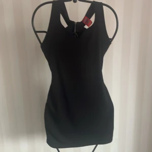 Svart ärmlös klänning - Snygg svart ärmlös klänning i tight passform. Perfekt för festliga tillfällen eller en utekväll. Klänningen har en stilren design med en unik ryggdetalj som ger en extra touch. Materialet känns bekvämt och smidigt mot huden.