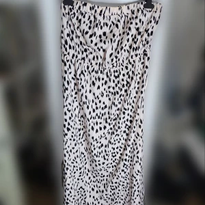 Svartrosa mönstrad långklänning - Långklänning i ljusrosa och svart med ett coolt mönster. Storlek 44/XL. Klänningen har en elastisk söm både över och under bysten för en bekväm passform som inte glider ner trots axelbandslös. Tror jag köpte den på bohoo. Inga defekter.