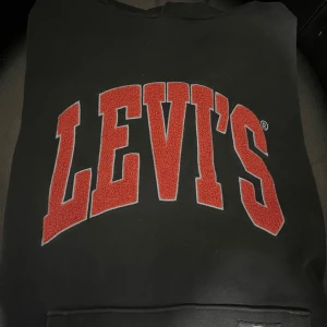 Svart hoodie från Levi's - Säljer en svart hoodie med fin luva från Levi's med stort rött logotryck på framsidan, storlek xs men passar defenetivt också s. Perfekt för en casual look och superbekväm att ha på sig. Passar både till vardags och chillkvällar, inget fel med den. Hör av dig om du är intresserad! 🖤