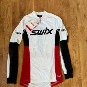 Oanvänd Långärmad underställströja från Swix - Säljer en helt oanvänd långärmad underställströja från Swix i vitt, rött och svart. Storlek S men passar även en XS. Perfekt som baslager när man åker skidor eller är ute i naturen. Har ett andningsbart material. Den har Swix-loggan tryckt på bröstet och ärmarna. Taggarna sitter fortfarande kvar! Nypris 599, säljer för 400 kr. 