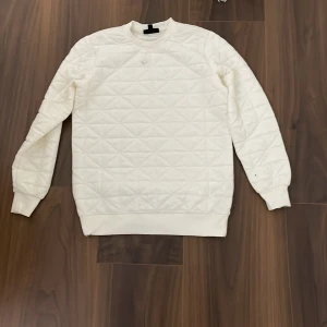 Vit quiltad tröja från SMOG - Säljer en stilren vit quiltad tröja från SMOG i storlek XS. Tröjan har en regular fit och är perfekt för både höst och vinter. Den är långärmad och har ribbade muddar vid ärmslut och nederkant. Superbekväm och lätt att matcha med allt! 🤍