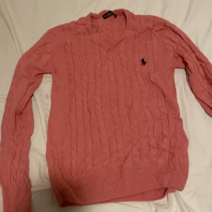 Rosa stickad tröja från Polo Ralph Lauren - Säljer en snygg rosa stickad tröja från Polo Ralph Lauren. Den har ett klassiskt kabelstickat mönster och en broderad logga på bröstet. Perfekt för både höst och vår, med långa ärmar och ribbade kanter. Superfin och i bra skick! 💖