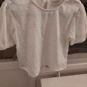 Vit blus från LC Waikiki - Söt vit blus från LC Waikiki med små blommiga detaljer. Den har puffiga trekvartsärmar och en rund halsringning. Perfekt för vår och sommar! 🌸