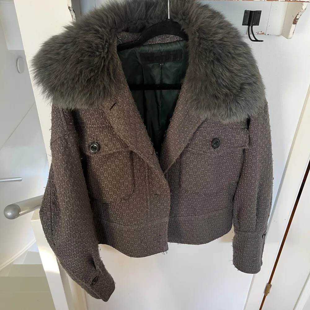 Säljer en superfin grå kappa från Meotine i storlek S/M. Den har en stor, fluffig pälsdetalj vid kragen och knappar framtill. Perfekt för höst och vinter, och ger en lyxig känsla. Passar både till vardags och festliga tillfällen.. Takit.