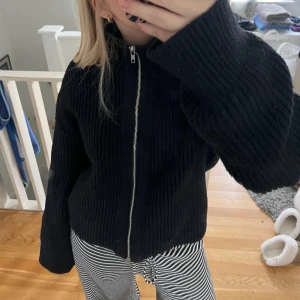 Svart stickad tröja med dragkedja - Säljer en svart stickad tröja med dragkedja framtill. Den har långa ärmar och en mysig, ribbad design som passar perfekt för höst och vinter. Tröjan är i bra skick och är superbekväm att ha på sig. Perfekt för att hålla sig varm och stilren under kyligare dagar.