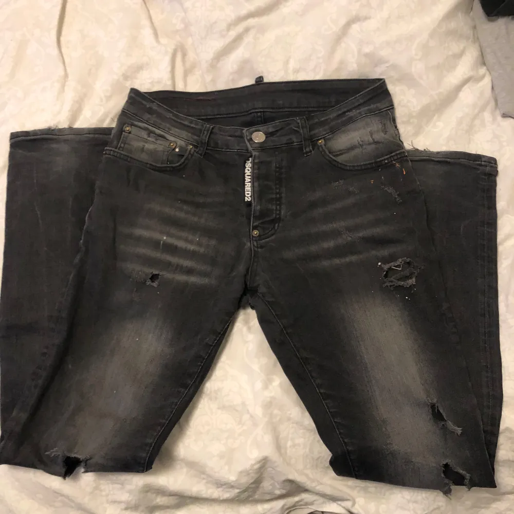 Säljer ett par svarta jeans från Dsquared2 i storlek 48. De har en cool, sliten look med flera revor och slitningar. Perfekta för en avslappnad och trendig stil. Tillverkade i Italien med hög kvalitet.. Jeans & Byxor.