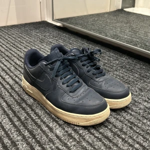 Mörkblå Nike Air Force sneakers - Säljer ett par mörkblå Nike Air Force sneakers i bra skick. De har en klassisk design med snörning och en ljus sula som ger en snygg kontrast. Perfekta för både vardag och fest! 🏀👟