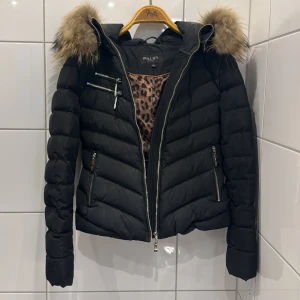 Svart dunjacka från Hollies - Fin kort dunjacka från Hollies i storlek 36 som passar perfekt till vintern, är varm och skön. Jackan är i fint skick, men använd så finns små tecken på anvädning. Nypris: ca 4000kr.