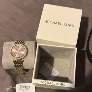 Guldfärgad klocka från Michael Kors - Säljer en snygg guldfärgad klocka från Michael Kors med en glittrig boett och rosa urtavla. Klockan kommer i originalförpackning och är i mycket bra skick. Perfekt för både vardag och fest! ✨