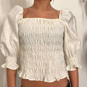 Vit blus med puffärmar - Säljer en superfin vit blus med puffiga trekvartsärmar och smockdetaljer. Den har en söt, rynkad design som ger en romantisk känsla. Perfekt för både vardag och fest! 💫