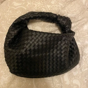 Svart flätad väska - Snygg svart väska i flätat mönster. Köpt på bohoo i somras å endast använd ett fåtal gånger! Säljer för 160kr