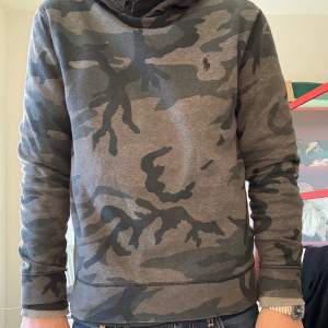 Säljer en grå Ralph Lauren camo tröja i bra skick. Perfekt för en avslappnad stil och passar till både vardag och chill. Den har en klassisk passform och är superbekväm. Perfekt för höst och vår!