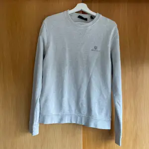 Säljer en stilren grå sweatshirt från Belstaff. Den har en klassisk rund hals och långa ärmar, perfekt för både vardag och avslappnade tillfällen. Materialet känns mjukt och bekvämt, och den diskreta loggan på bröstet ger en snygg touch. Passar perfekt till jeans eller chinos!