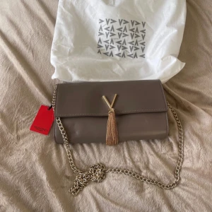 Beige axelväska från Valentino - Snygg beige axelväska från Valentino i mycket bra skick. Väskan har en elegant kedjerem och en dekorativ tofsdetalj framtill. Perfekt för både vardag och fest! 👜✨