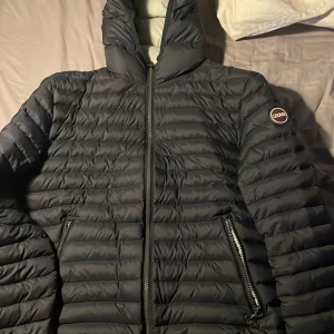 Marinblå från Colmar - Säljer en snygg svart dunjacka från Colmar i mycket bra skick. Jackan har en dragkedja framtill och två praktiska fickor med dragkedjor. Perfekt för kyliga höst- och vinterdagar. Den är långärmad och har en stilren design med Colmar-logga på ärmen.