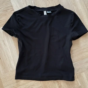 Svart kortärmad topp från H&M Divided - Säljer en svart kortärmad topp från H&M Divided i storlek S. Toppen är enkel och stilren, perfekt för vardagsbruk eller att matcha med olika outfits. Den är i bra skick och gjord av mjukt material för en bekväm passform.