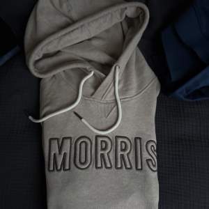 Säljer en snygg beige hoodie från Morris i bra skick. Den har en stor logga på bröstet och en praktisk magficka. Perfekt för höst och vår, med långa ärmar och en skön huva med dragsko. Passar både till vardags och chillkvällar.