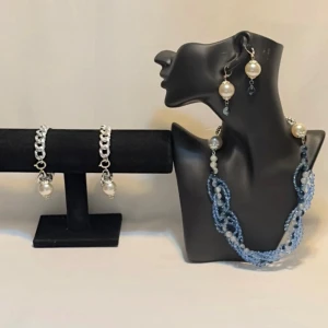 Smyckeset med pärlor och blå detaljer - Snyggt smyckeset med halsband, armband och örhängen. Halsbandet har blå och silverfärgade pärlor i olika nyanser och storlekar. Armbandet och örhängena har stora vita pärlor och silverkedjor. Perfekt för att piffa upp en outfit till fest eller speciella tillfällen.Ett par örhängen och ett par armband plus en halsband handgjorda mycket mycket fint nytt oanvänd 