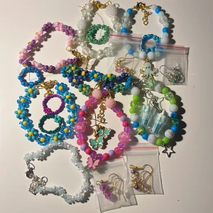 19 Färgglada armband och örhängen - Säljer ett set med färgglada armband och örhängen. Armbanden har pärlor i olika färger som rosa, blå, grön och vit, med detaljer som fjärilar och blommor. Örhängena är i guld och silver med stjärnor och andra söta detaljer. Perfekt för att liva upp vilken outfit som helst!