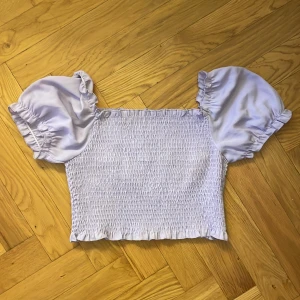 Ljuslila smockad topp - Säljer en superfin ljuslila topp med smockad kropp och puffiga korta ärmar. Perfekt för sommardagar eller en festlig kväll. Toppen har en söt volangdetalj vid ärmslut och nederkant. Passar perfekt till både jeans och kjol! Köptes på Gina tricot för två år sedan för 499, är använd några gånger men är i väldigt bra skick💞