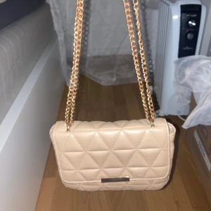 Beige väska - Säljer en superfin beige väska. Perfekt för både vardag och fest. Kedjan har tappat lite färg men annars man märker inte så mkt! Säljer pga av att jag inte använder den längre. Fint skick🩷