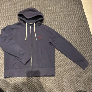Mörkblå hoodie från Ralph Lauren - Säljer en snygg mörkblå zip up hoodie från Ralph Lauren. Storlek M men passar även S, i fint skick och säljs för ett bra pris!