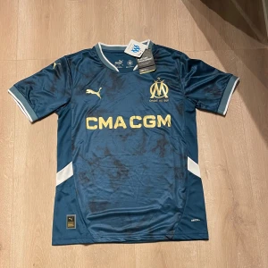 Marseille tröja  - Säljer en replika av Olympique Marseilles bortatröja 24/25, storlek S. Tröjan är i perfekt skick, aldrig använd och har alla originaltaggar kvar.