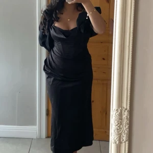 Svart långklänning med draperad detalj - Elegant svart långklänning med draperad detalj och en smickrande passform. Perfekt för festliga tillfällen. Klänningen har en vacker design som ger en sofistikerad look. ANVÖND ENDAST VID TVÅ TILLFÄLLEN! Köpt från booho 