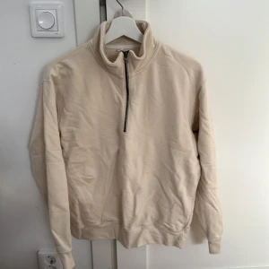 Beige tröja med dragkedja från Uniqlo - Säljer en stilren beige tröja från Uniqlo i storlek S. Den har en praktisk dragkedja vid halsen och är perfekt för både höst och vår. Tröjan är i bra skick och passar till många olika outfits. Perfekt för en casual look! 🍂