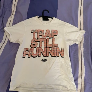 Syna world T shirt - Säljer en vit synna world t shirt med texten 'TRAP STILL RUNNIN'