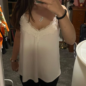 Vit linne med spetsdetaljer - Säljer ett superfint vitt linne med vackra spetsdetaljer vid halsringningen. Perfekt för sommardagar eller vardagligt. Linnet har smala axelband och en lös passform som ger en luftig känsla. Passar både till vardags och fest!