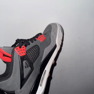Air Jordan 4 Retro i grå och röd - Säljer ett par Air Jordan 4 Retro i mörkgrått med svarta och infraröda detaljer. Skorna är i mycket bra skick. Perfekta för både vardag och fest! Jag har köpt dom för 5000kr helt nya