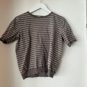 Brun och vit randig tröja från H&M - Säljer en snygg grå och vit randig tröja från H&M i storlek M. Tröjan har korta ärmar och är perfekt för både vår och sommar. Den är i bra skick och passar till många olika outfits. Perfekt för en avslappnad stil!