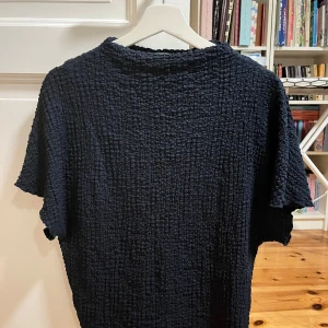 Mörkblå t-shirt topp från Zara - Säljer en mörkblå t-shirt från Zara i storlek S. Den har en cool texturerad yta som ger en unik look. Perfekt för både vardag och fest! Toppen är kortärmad och gjord i ett bekvämt material. Passar perfekt till jeans eller kjol.