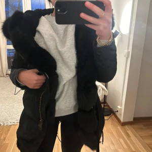 Svart parkajacka med pälsdetaljer - Säljer en snygg svart parkajacka med pälsdetaljer på huvan. Jackan har en dragkedja framtill och är perfekt för kyliga dagar. Den är i mycket bra skick och passar perfekt för höst och vinter. Supermysig och stilren!