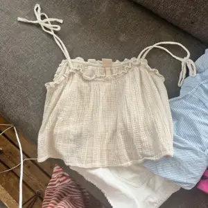 Säljer en söt vit ärmlös topp från H&M i storlek 36. Toppen har tunna axelband som knyts och en volangdetalj vid halsringningen. Perfekt för sommardagar eller en avslappnad utflykt. Materialet är lätt och luftigt, vilket gör den bekväm att bära. 🏖️