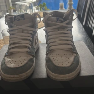 Nike Air sneakers i grått och vitt - Säljer ett par Nike Air sneakers i grått och vitt. De har en klassisk hög modell med snörning och är i bra skick. Perfekta för både vardag och träning. Skorna har en snygg kombination av grå mocka och vitt syntetmaterial. (Har tyvärr inte den rätta boxen)