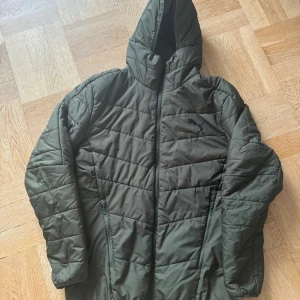 Grön dunjacka från Puma - Säljer en grön dunjacka från Puma i storlek M. Jackan har en quiltad design med dragkedja och huva, perfekt för kyliga dagar. Den är i mycket bra skick och har en stilren look med Puma-loggan på bröstet. Perfekt för höst och vinter!
