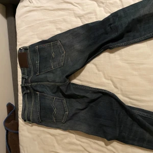 Mörkblå jeans från Replay - Säljer ett par mörkblå Replay Anbass jeans i bra skick. De har en klassisk femficksdesign och en snygg tvätt som passar perfekt till både vardag och fest. Jeansen är i storlek 32 och har en bekväm passform. Perfekta för höst och vår!