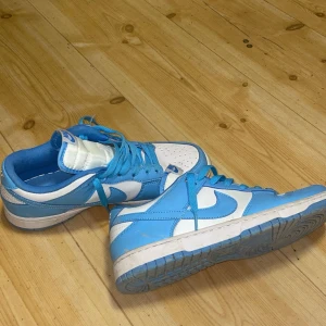 Nike Dunk i blått och vitt - Säljer ett par Nike Dunk sneakers i blått och vitt. De har en klassisk design med snörning och en bekväm passform. Skorna är i bra skick med lite slitage på sulan. Perfekta för både vardag och träning! Ska såklart rengöras 