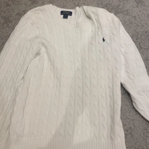 Vit stickad tröja från Polo Ralph Lauren - Säljer en klassisk vit stickad tröja från Polo Ralph Lauren. Den har ett snyggt kabelstickat mönster och den ikoniska loggan broderad på bröstet. Perfekt för både höst och vinter, med långa ärmar och ribbade kanter. Supermysig och stilren! Storlek är XL men den passar väldigt bra på folk som är 174cm upp till 183cm
