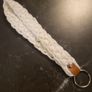 Vit virkad nyckelring - Snygg och unik vit virkad nyckelring med en liten läderdetalj och metallring. Virkad i 100% bomull. Perfekt för att hålla koll på dina nycklar med stil 😊 Den är handgjord och har en bohemisk känsla. Passar perfekt som en liten present eller för att piffa upp din egen nyckelknippa.